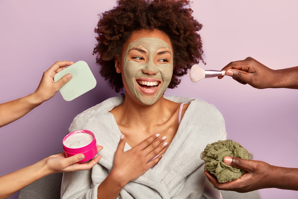 beautiful-refreshed-cheerful-woman-with-nourishing-clay-mask-looks-happily-aside-being-treated-by-cream-sponges-makeup-brush